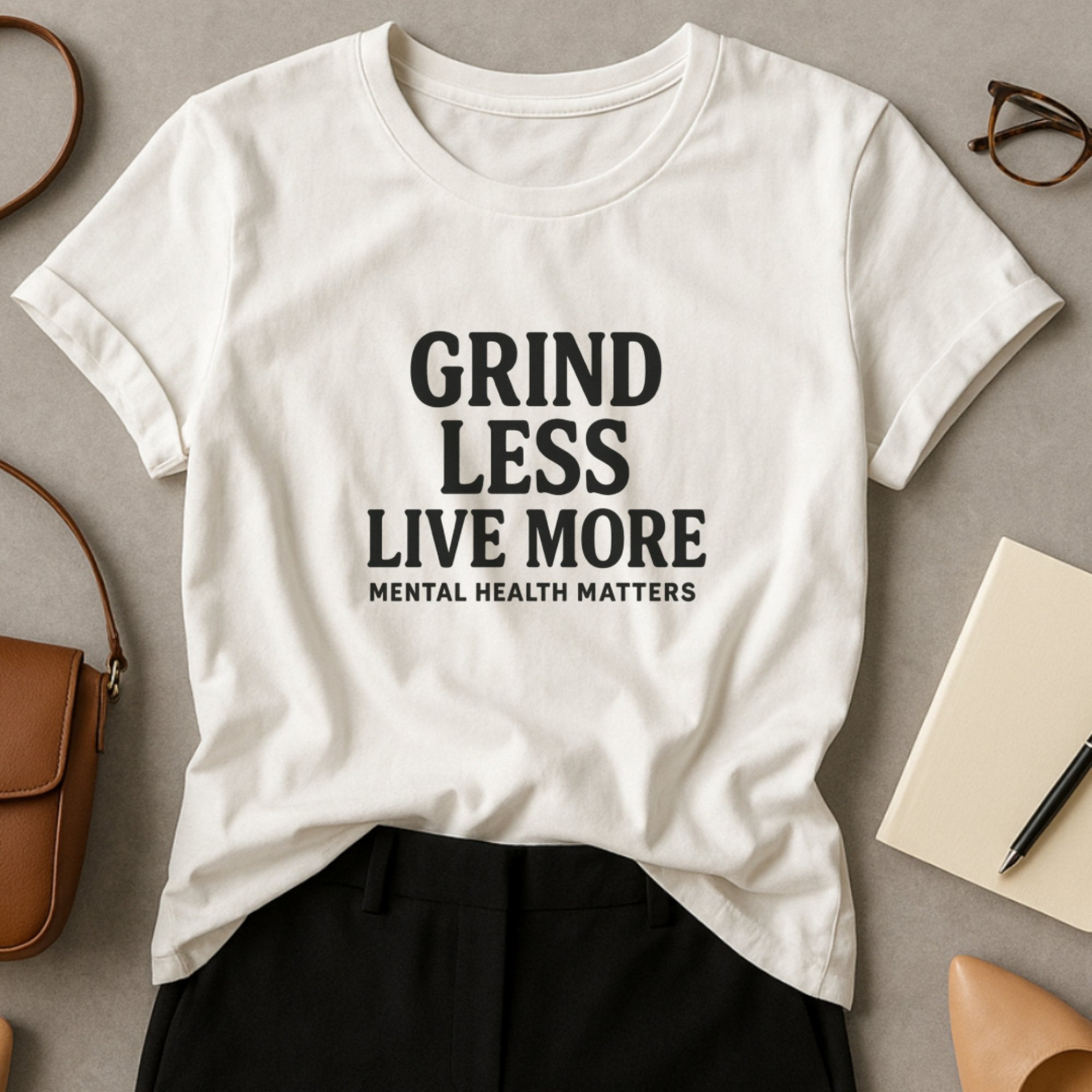 White mental health awareness t-shirt with bold typography saying “Grind Less, Live More – Mental Health Matters,” encouraging balance, rest, and a healthier approach to life