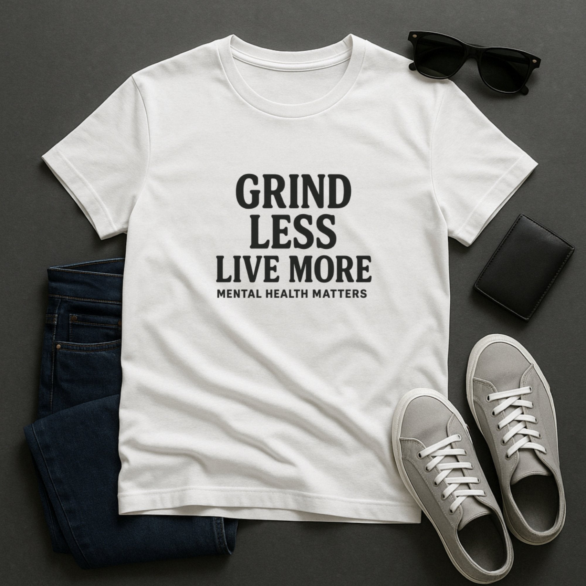 White mental health awareness t-shirt with bold typography saying “Grind Less, Live More – Mental Health Matters,” encouraging balance, rest, and a healthier approach to life