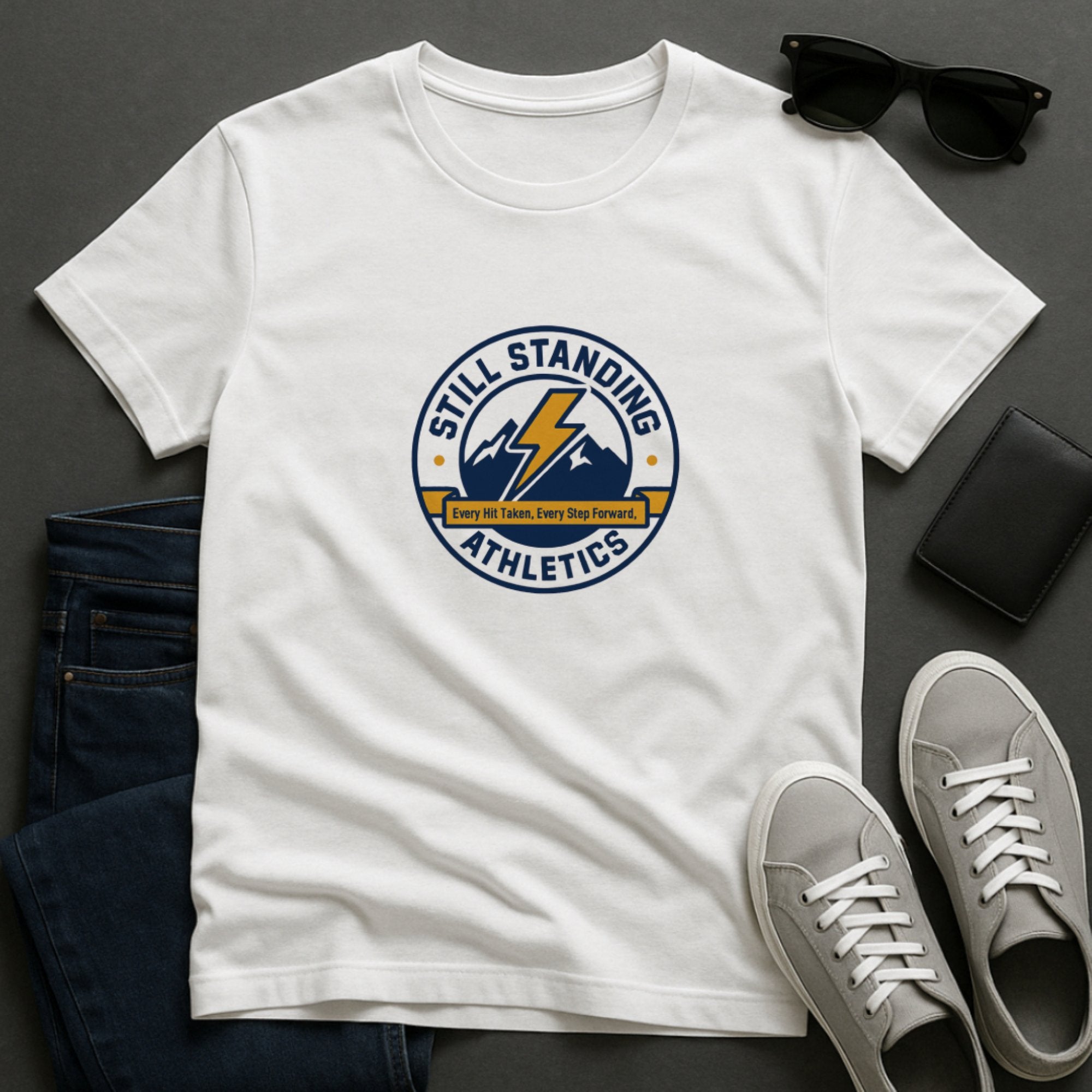 White “Still Standing Athletics” t-shirt with a bold lightning bolt over mountain peaks and the phrase “Every Hit Taken, Every Step Forward,” symbolizing strength, resilience, and pushing through challenges