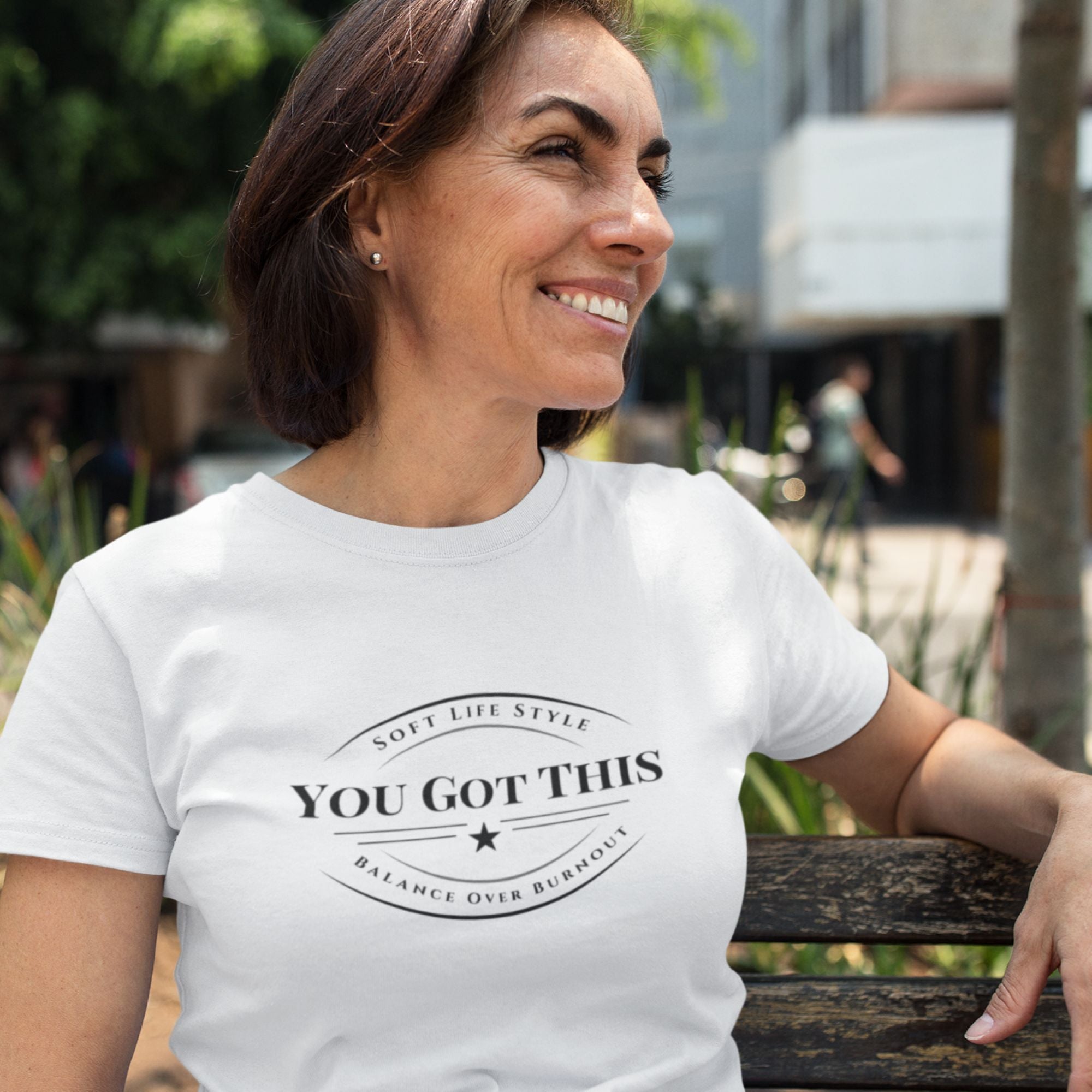 Woman wearing a white t-shirt with 'You Got This' text, sitting outdoors.