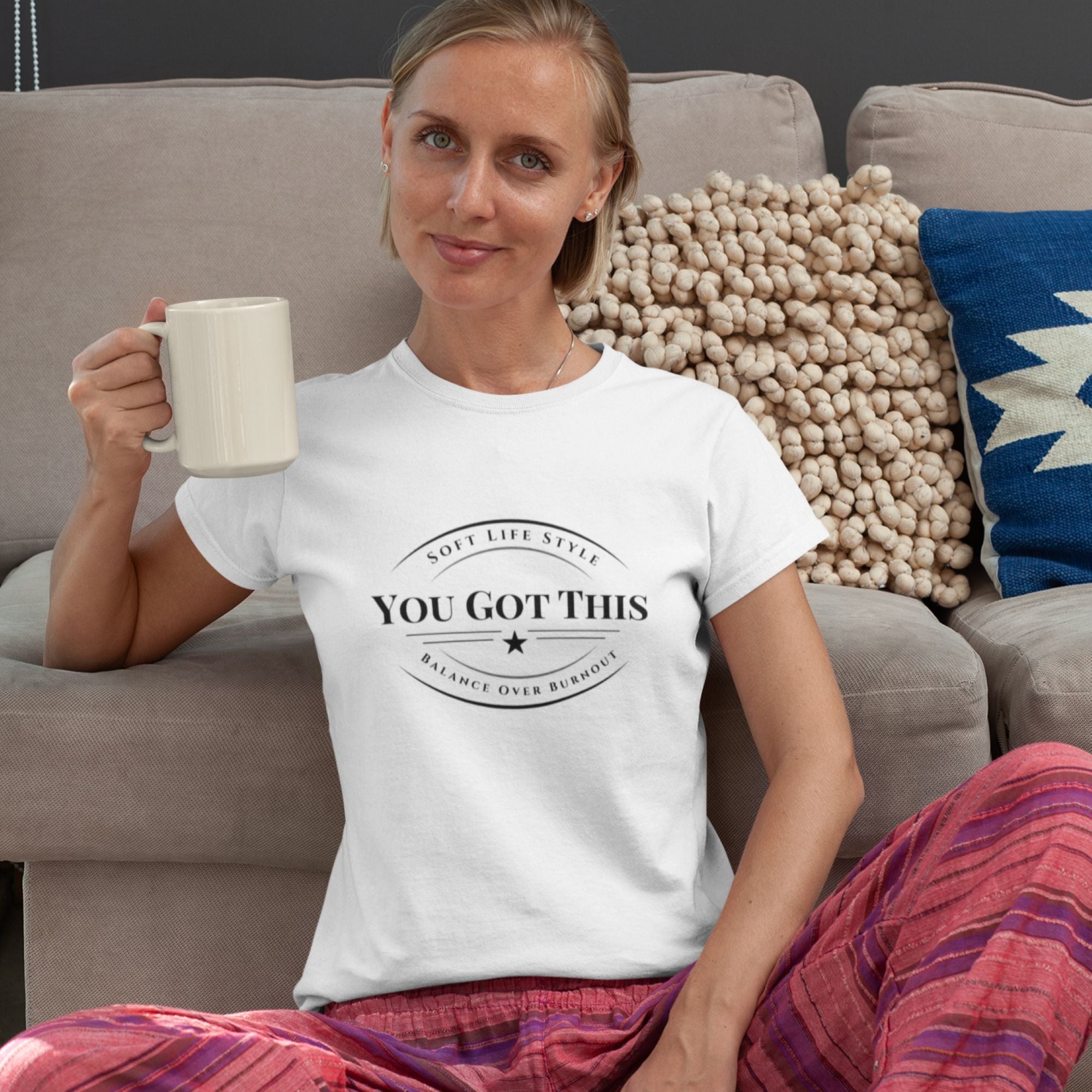 Woman wearing a white t-shirt with 'YOU GOT THIS' text, sitting on a couch holding a mug.