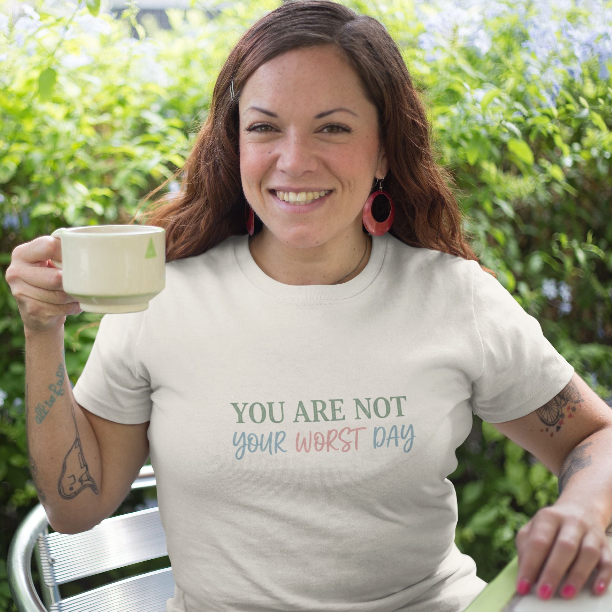 Woman wearing a t-shirt with motivational text, holding a mug outdoors.