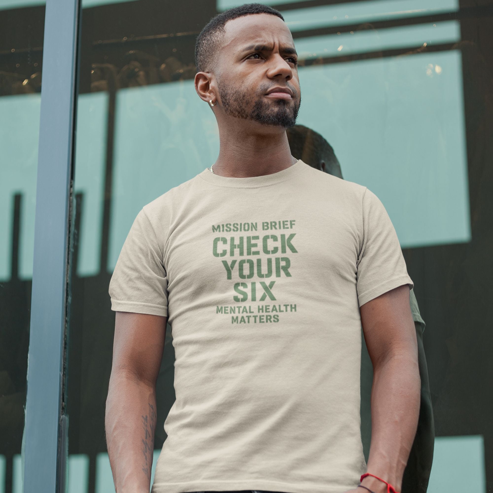 Man wearing a beige t-shirt with motivational text in front of a glass building.