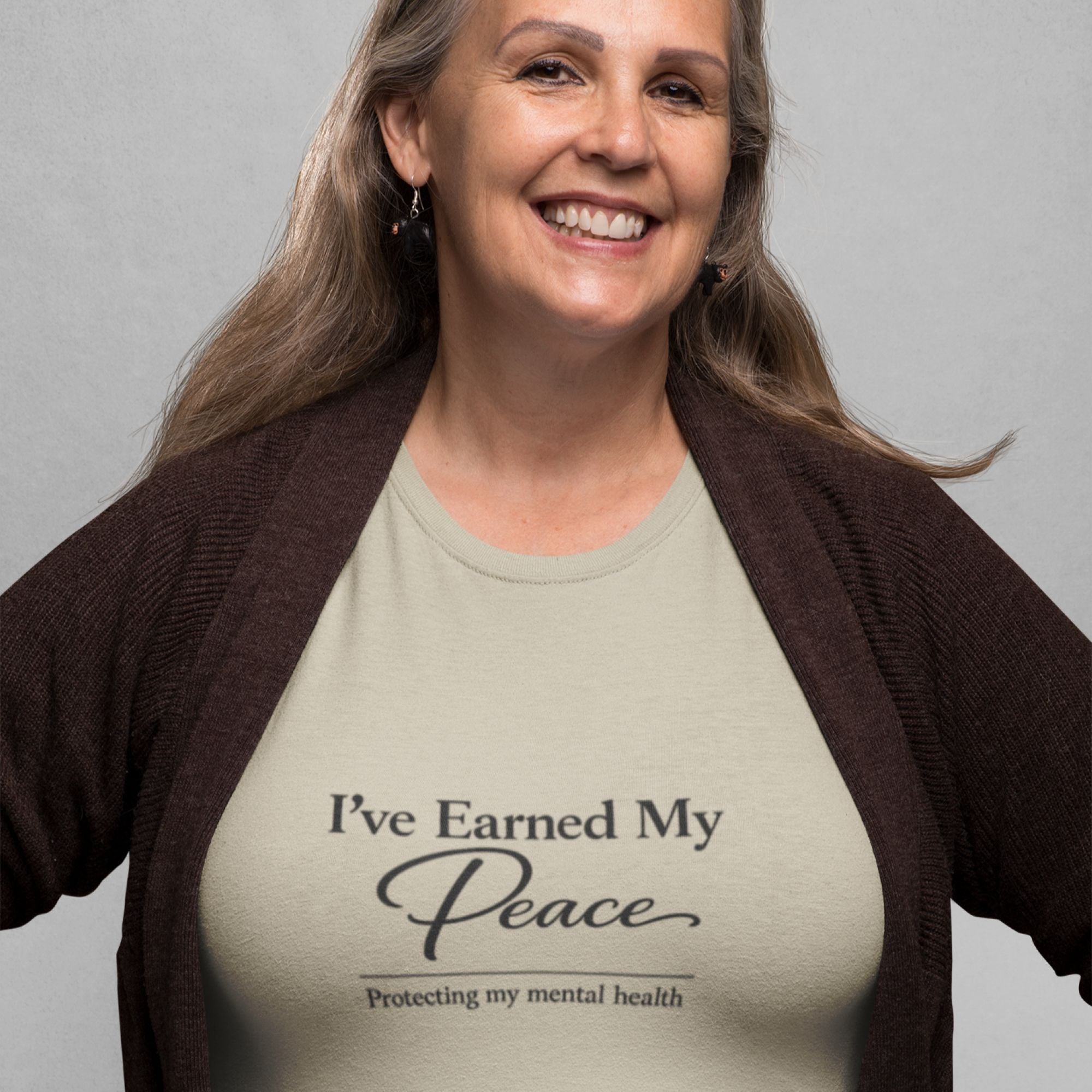 Tan minimalist t-shirt featuring the phrase “I’ve Earned My Peace” in elegant black typography, styled in a flat lay with coffee, book, glasses, and neutral lifestyle accents