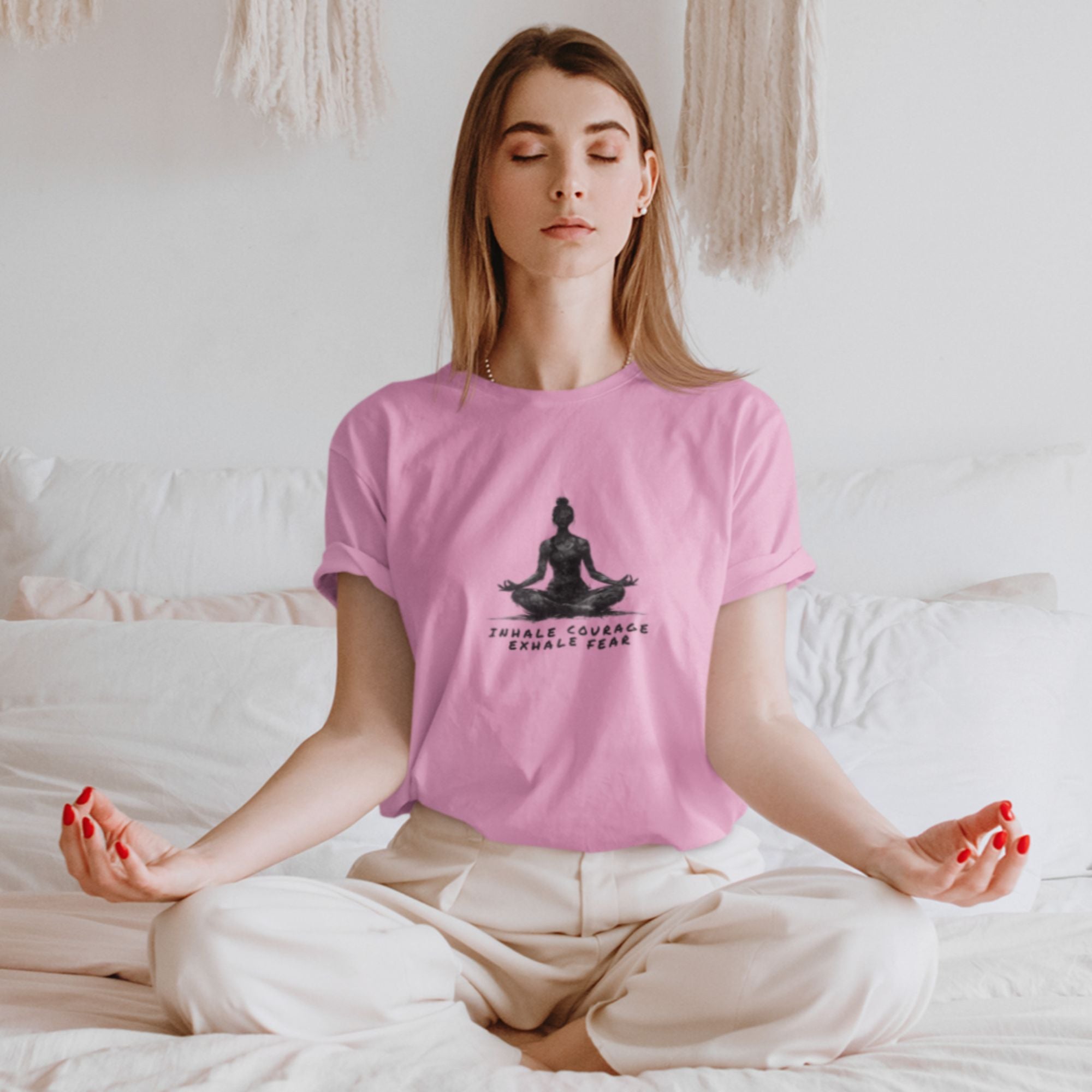 Woman meditating on a bed wearing a pink t-shirt with a yoga design.