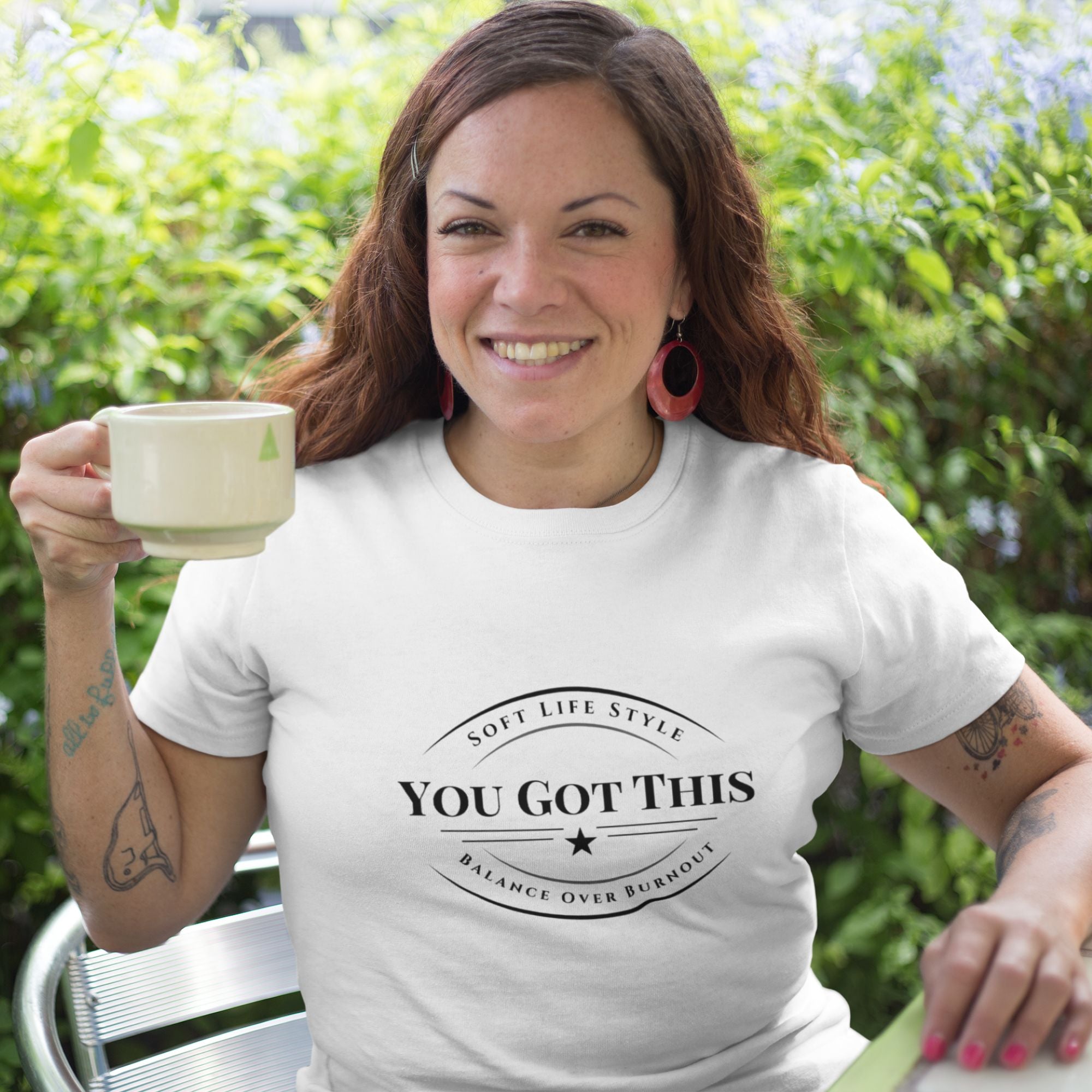 Woman wearing a white t-shirt with 'You Got This' text, holding a mug outdoors.
