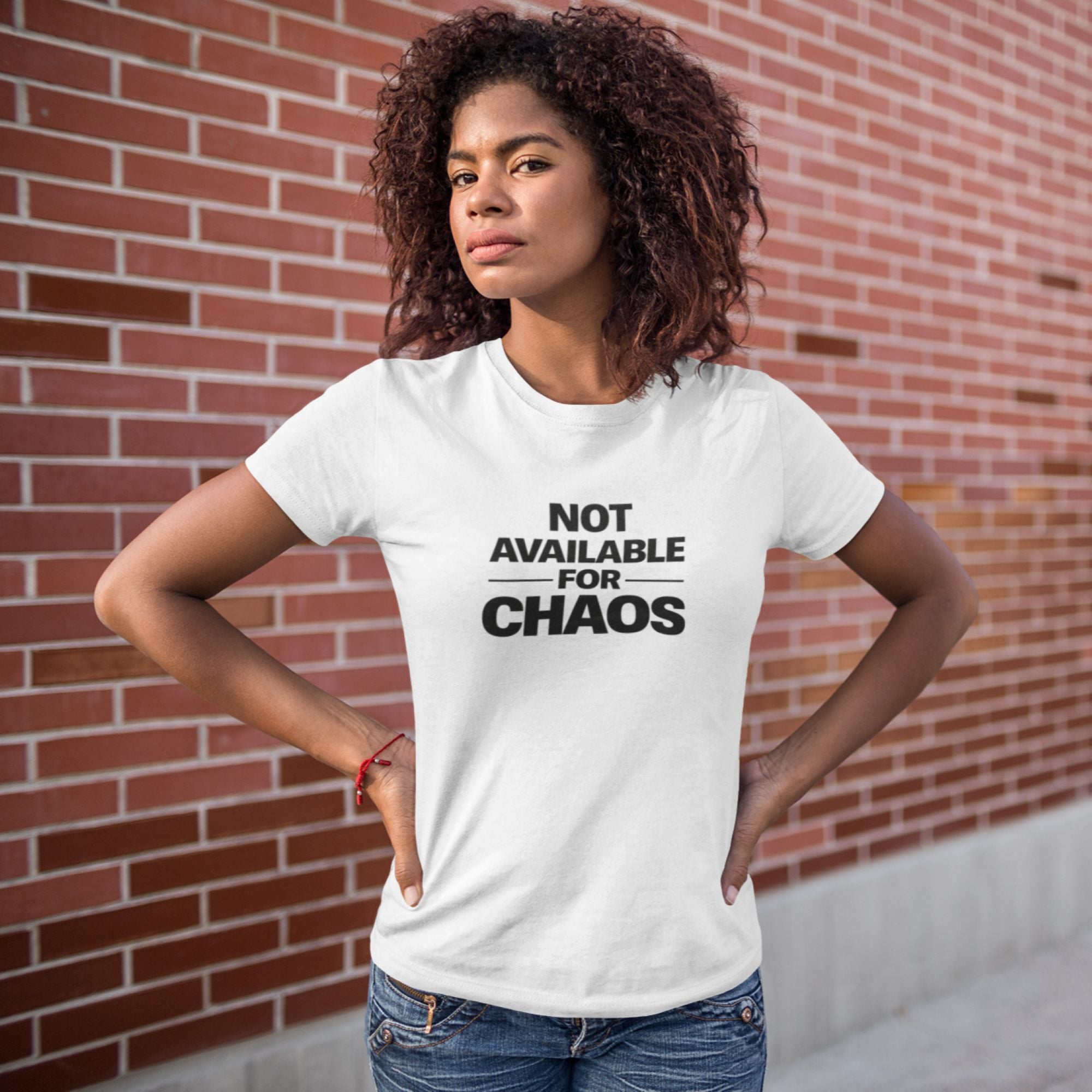 Person wearing a white t-shirt with 'Not Available for Chaos' text against a brick wall.