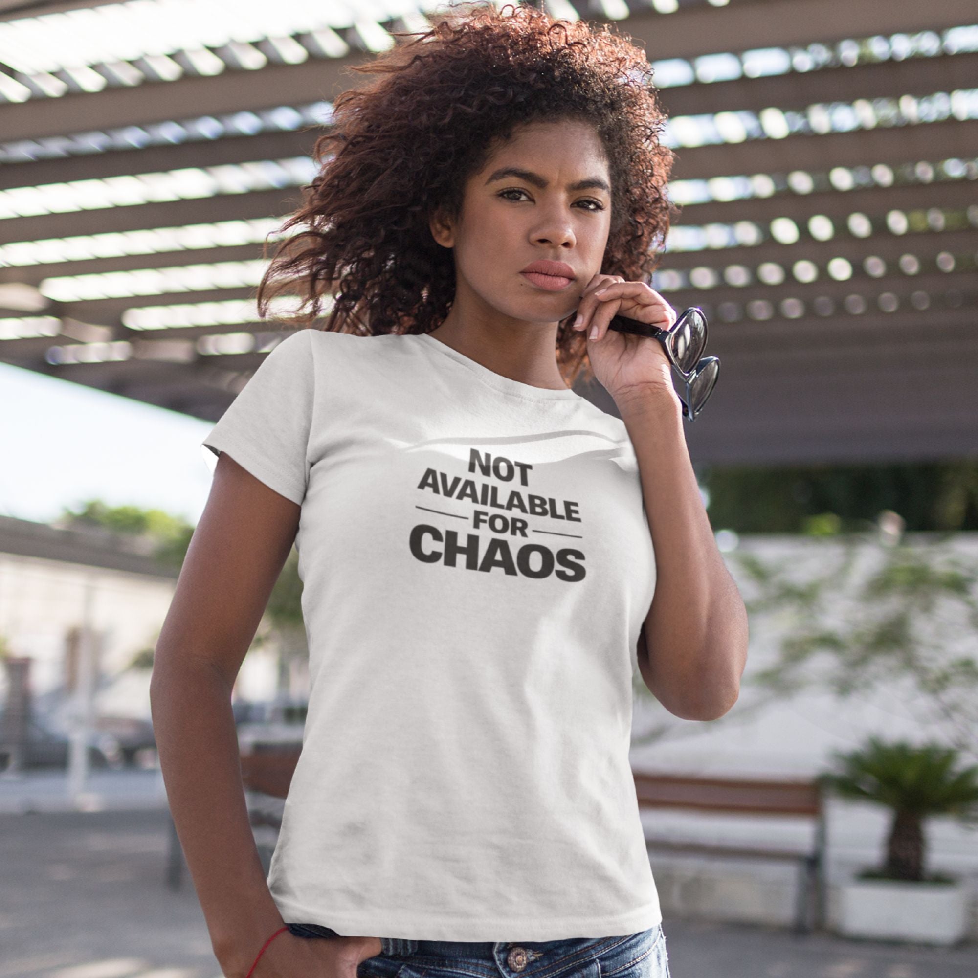 Woman wearing a white t-shirt with 'Not Available for Chaos' text outdoors.