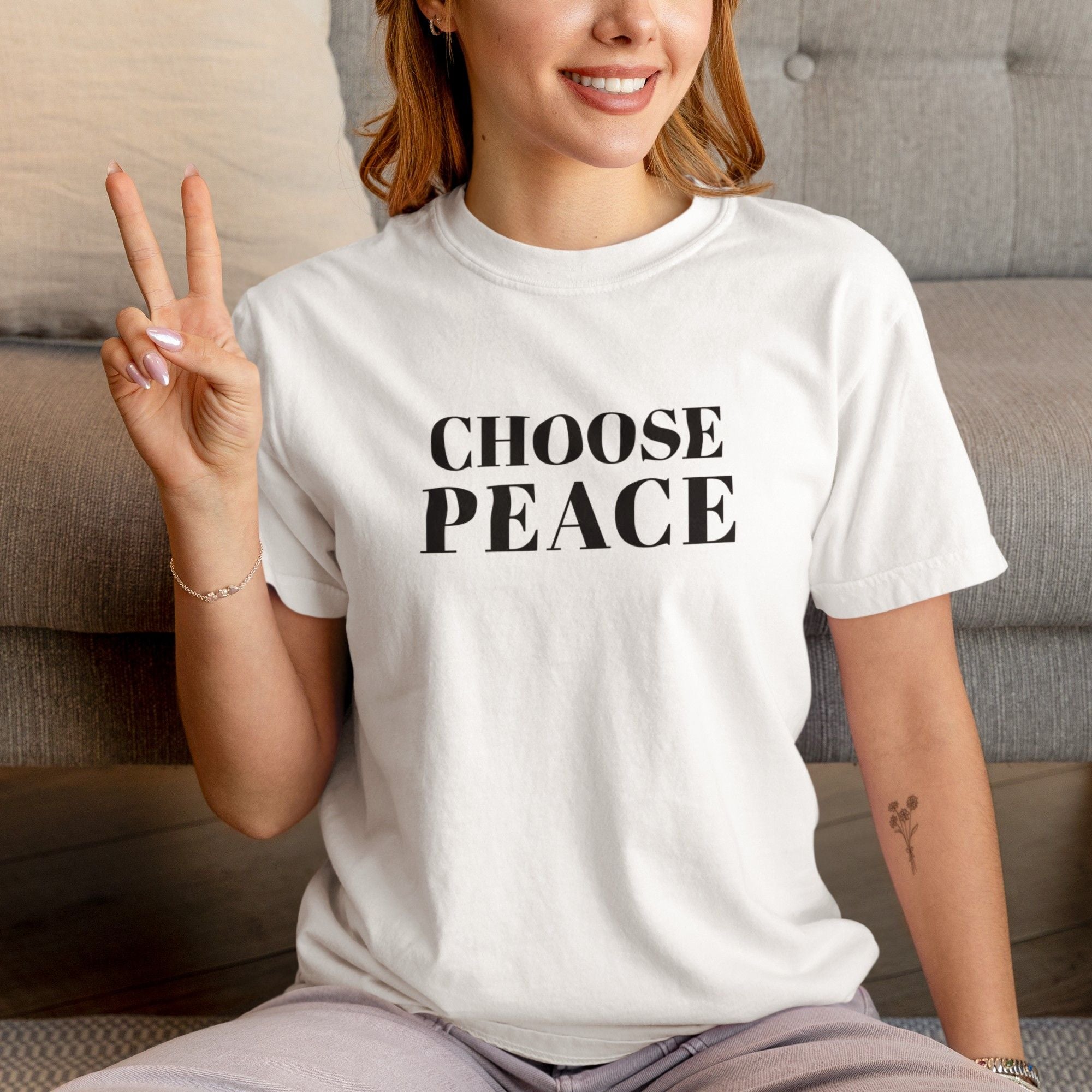 Person wearing a white t-shirt with 'CHOOSE PEACE' text, making a peace sign.