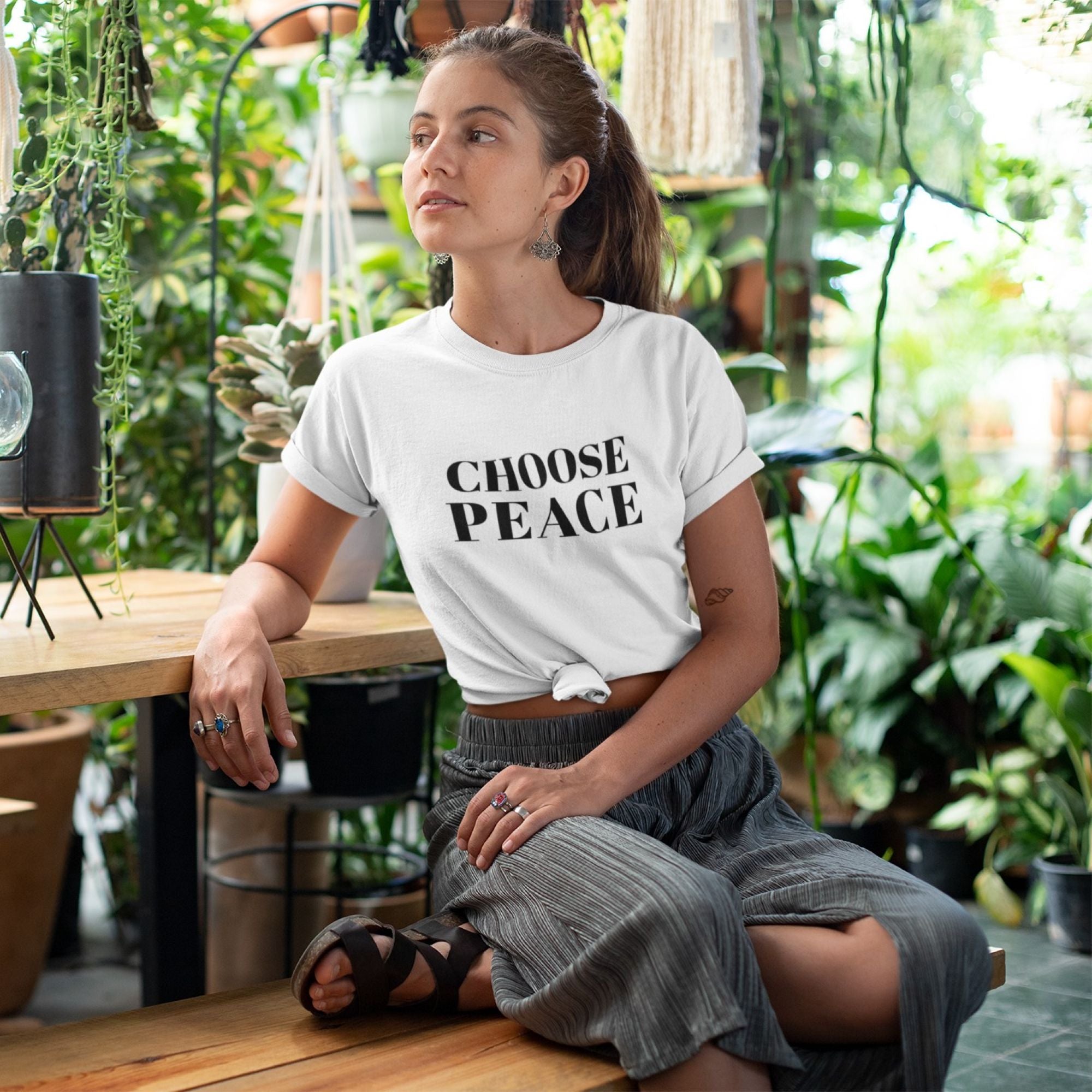 Woman wearing a 'CHOOSE PEACE' t-shirt in a lush green indoor setting.